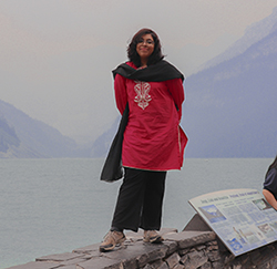 Image of Shaiza Hashmi smiling at camera standing on a wall in front of Lake Louise