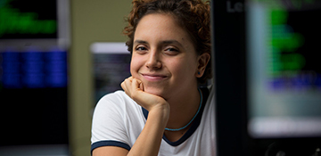 Woman student smiling at camera from behind a computer with code displayed on screen