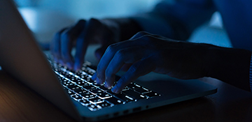 Dark room with person typing on lit-up keyboard