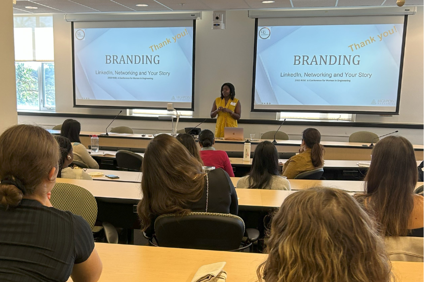 Young leader in the STEM field is presenting in front of a projector screen to a group of young ladies