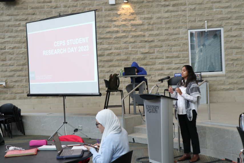 Young woman giving speaking to crowd gathered for research presentation.