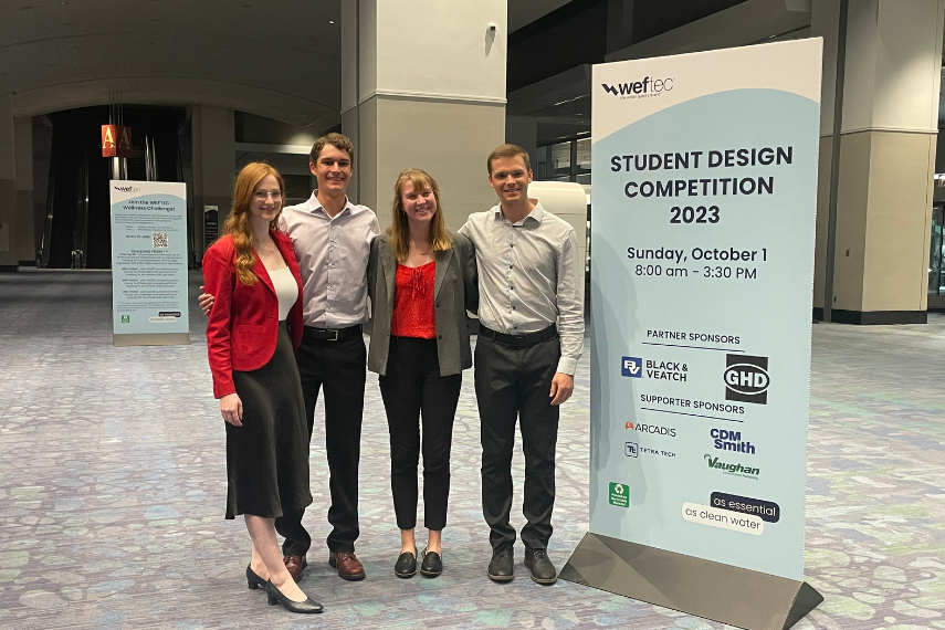 4 students (2 men and 2 women) standing beside banner in a conference lobby.