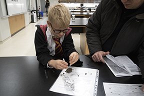 boy with tweezers picking apart a brown owl pellet dressed as Harry Potter