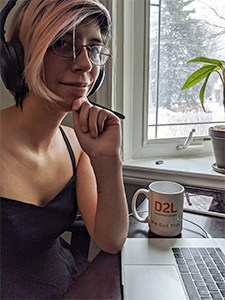 Zina Ramirez working from home with headphones on and D2L mug nearby.