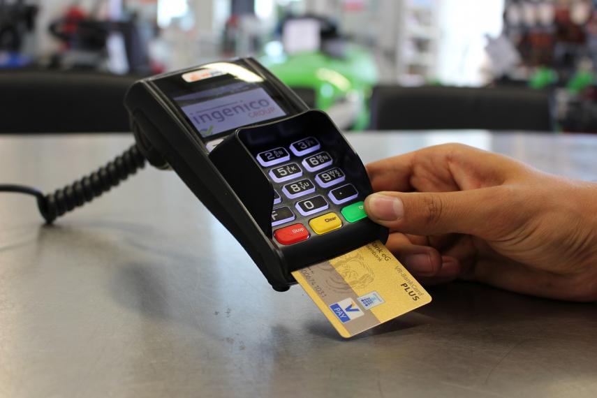 Image of person's hand holding pay terminal with debit or credit card inserted