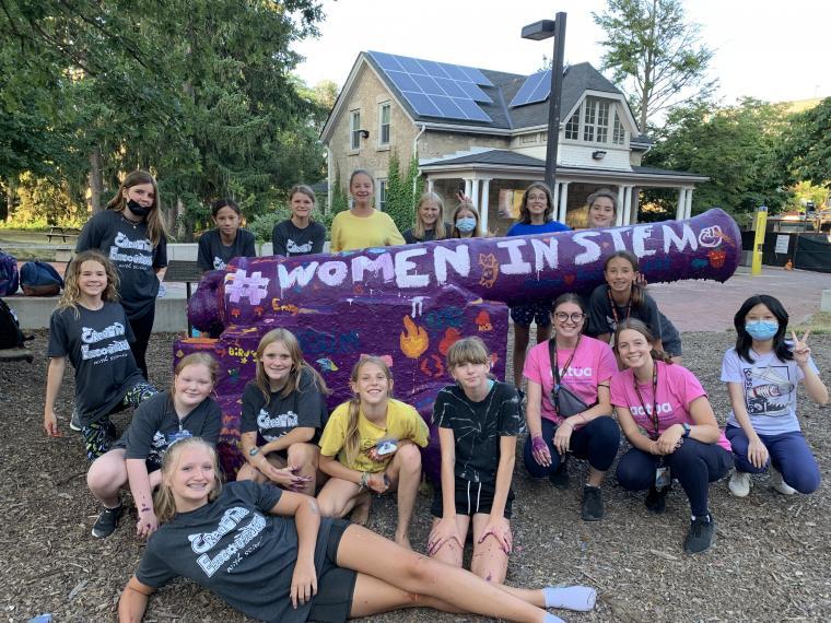 Several creative encounters summer campers pose in front of the U of G cannon, freshly painted purple with #WomenInSTEM