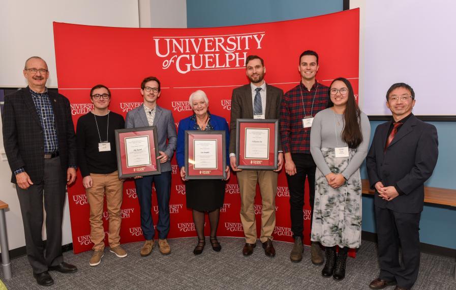 Group of award winners and faculty standing in front of U of G banner