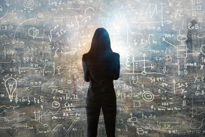 Silouette of a woman standing in front of a blackboard with mathematical equations written on it.