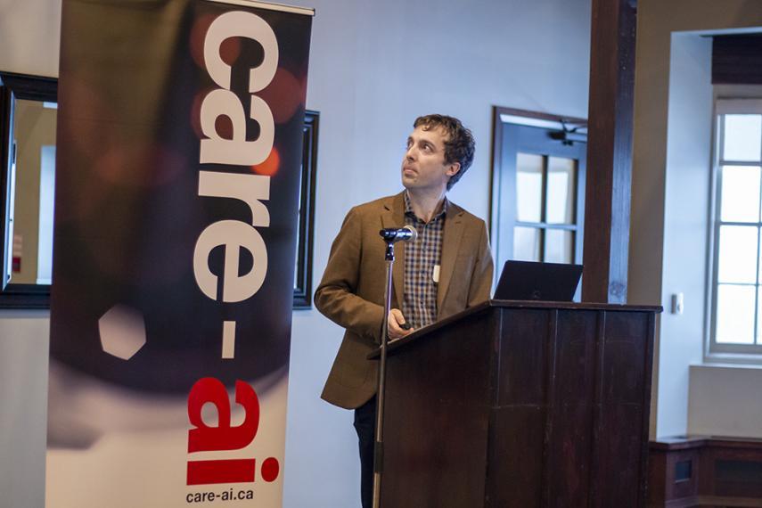 Graham standing at a podium looking at screen with care-ai banner to his left