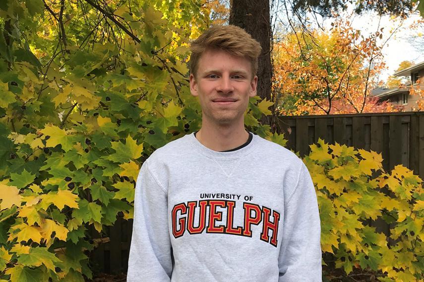Image of Grant Doherty wearing a grey University of Guelph sweater with trees in background
