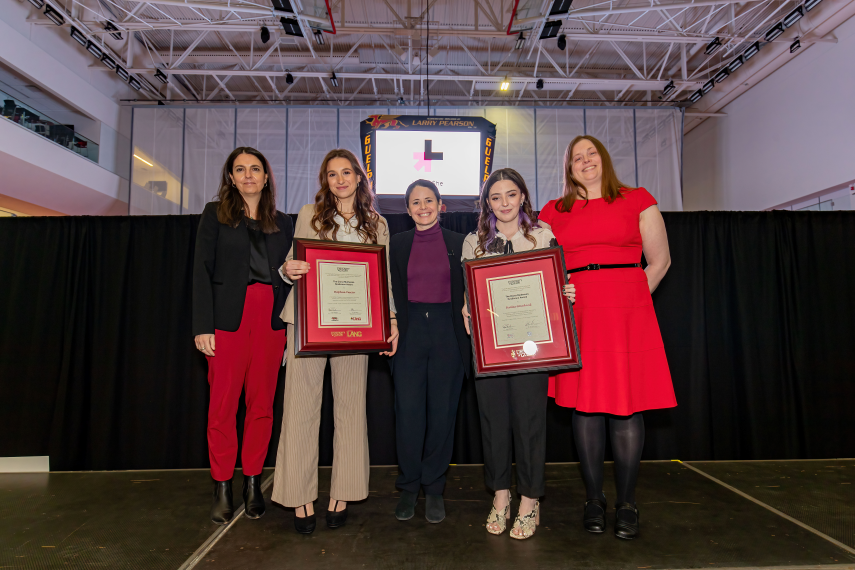 Five women stand on stage presenting awards smiling to camera