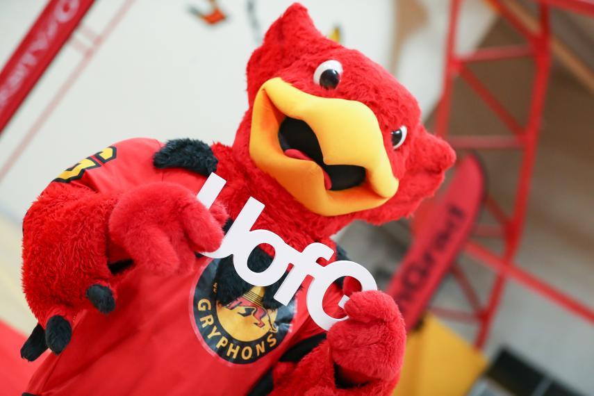 Image of Guelph Gryphon holding small "UofG" letter sign in large open area