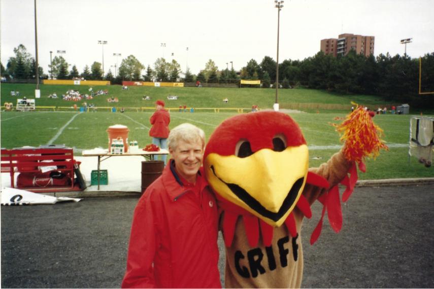 Man is standing at a football field with a mascot