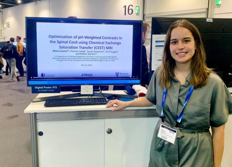 Alicia Cronin is standing with a computer that is also a digital poster at an event