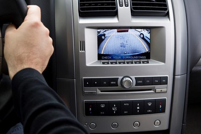 Image of a vehicle rearview camera with a hand on a steering wheel.