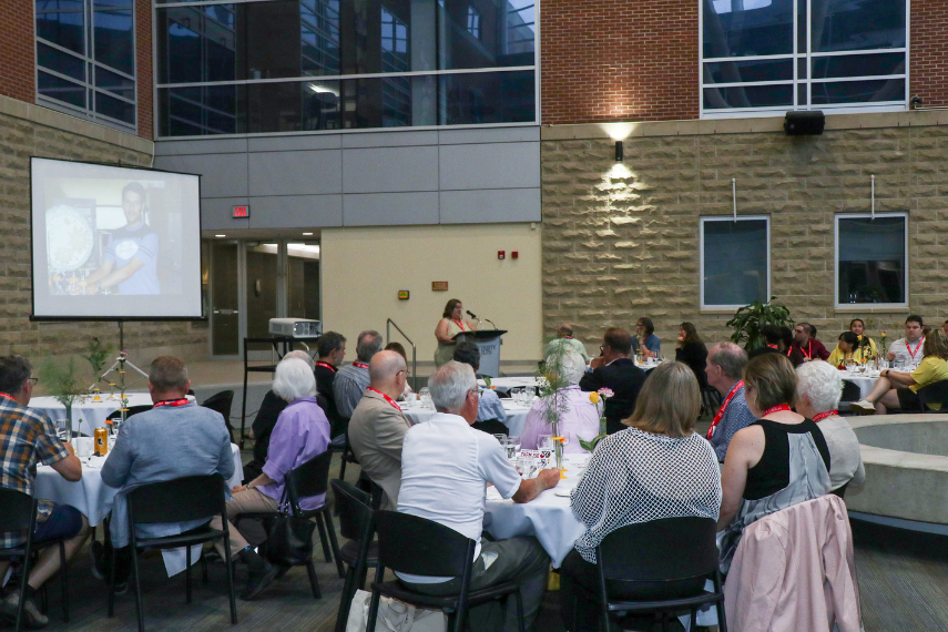 Group of Alumni at dinner, looking at speaker on podium.