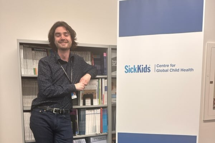 Cole Heasley smiles in front of sick kids banner