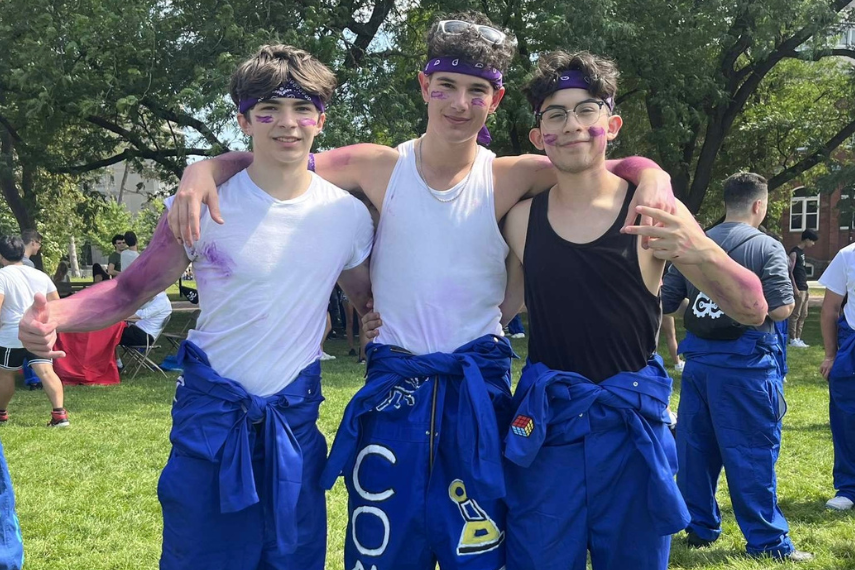 Three male students standing together outside at event, smiling to camera