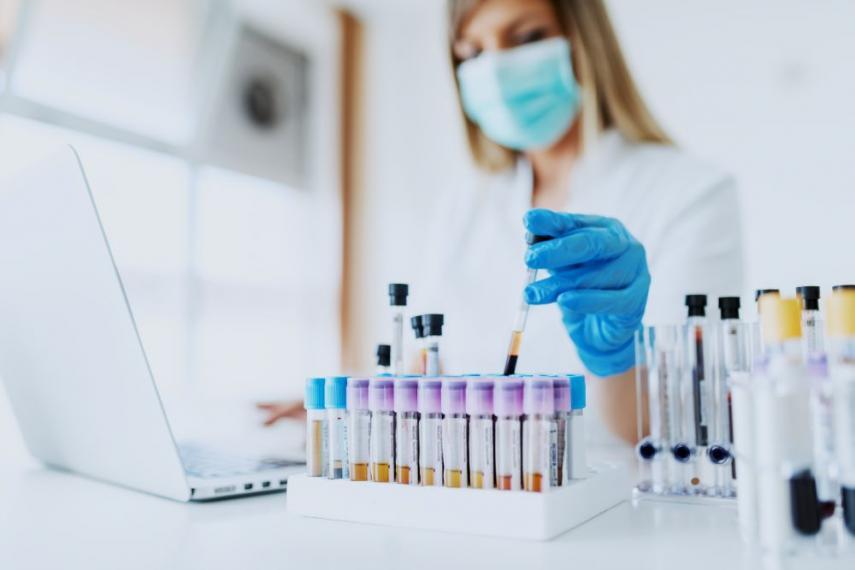 Woman in a lab wearing a mask and working with test tubes.