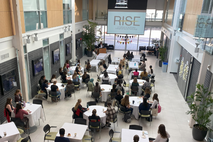 Group of women sitting at tables listening to the opening remarks in Thornborough building at the University of Guelph's RISE Conference.
