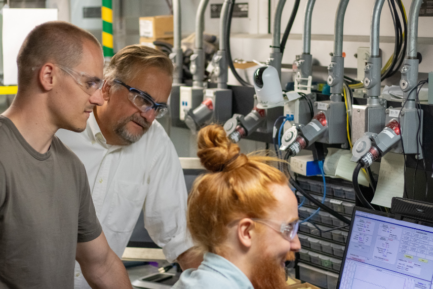 Dr. Marcel Schlaf and his two team members reading data on a monitor with safety glasses on