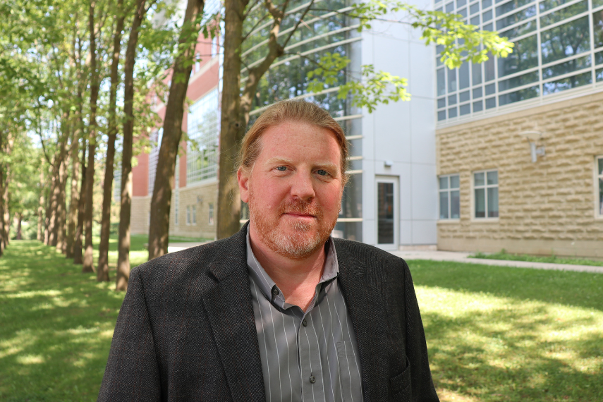 Man standing outside with trees and building behind him