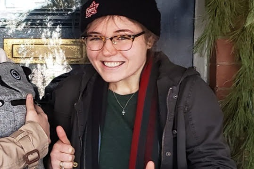 Girl wearing glasses and a hat smiling at camera with thumbs up 