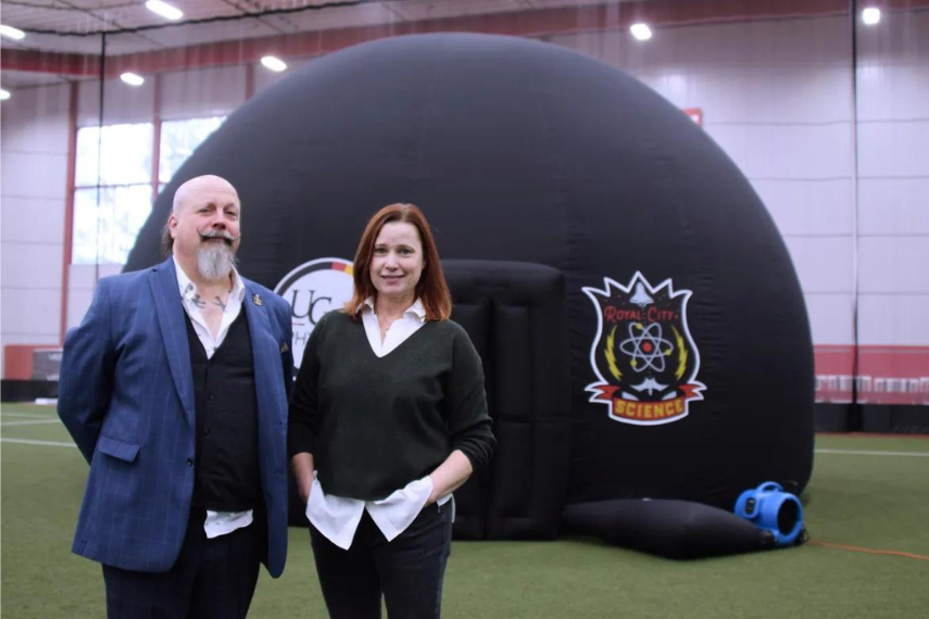 Orbax and Dr. O'Meara in front of inflatable black planetarium on turf field. 