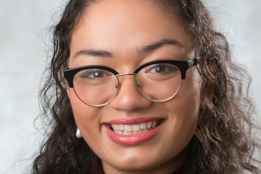 close up headshot of woman with curly hair and glasses smiling at camera.