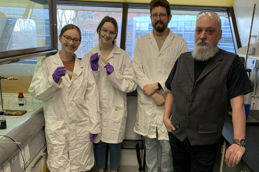 Researchers in lab coat smiling in lab with samples and Dr. Mario Monterio.