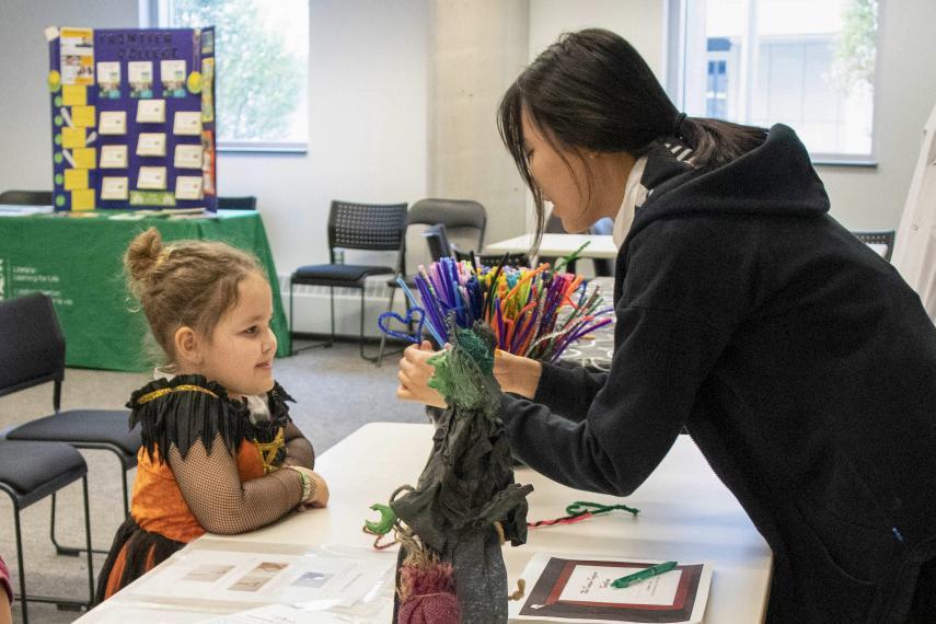 Volunteer leans over desk and shows younger school-aged girl science activity