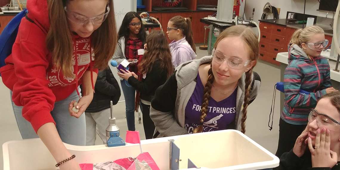 3 Girls gather around a science experiment.