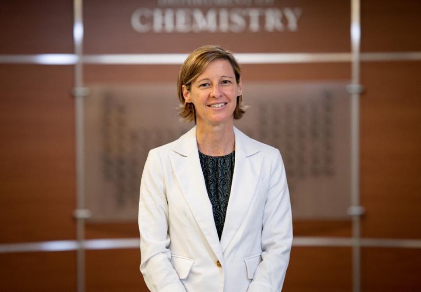 Woman standing in lab coat in front of wood wall