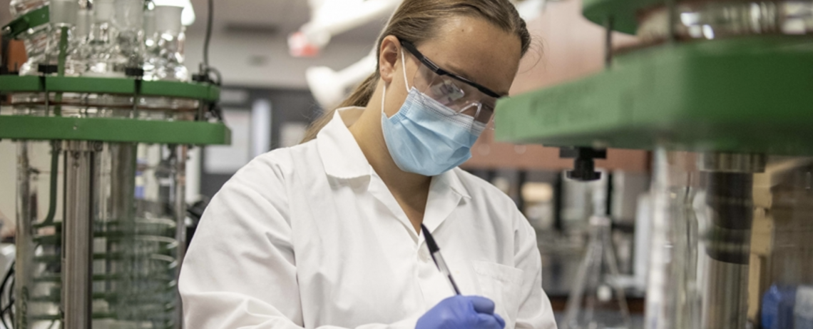 Co-op student in engineering lab working on essential COVID-19 research wearing full PPE