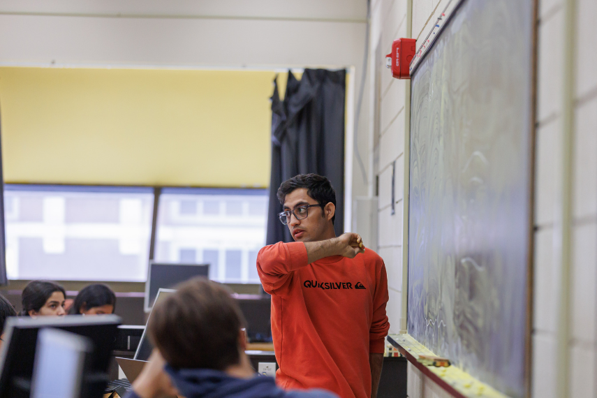 Man in red sweater looking at classroom about to write on a chalk board