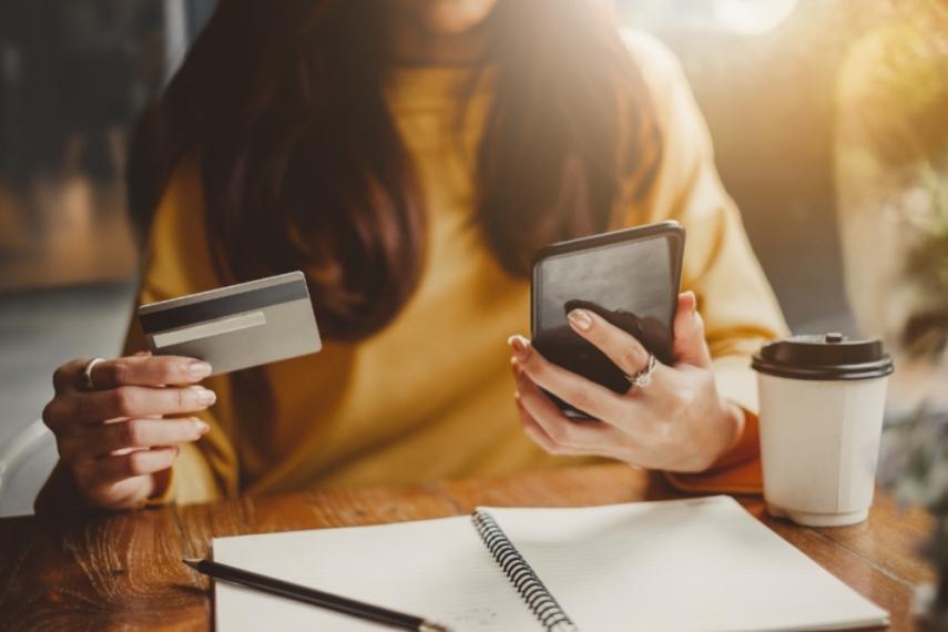 Woman sitting in a coffee shop purchasing something with your credit card on her phone