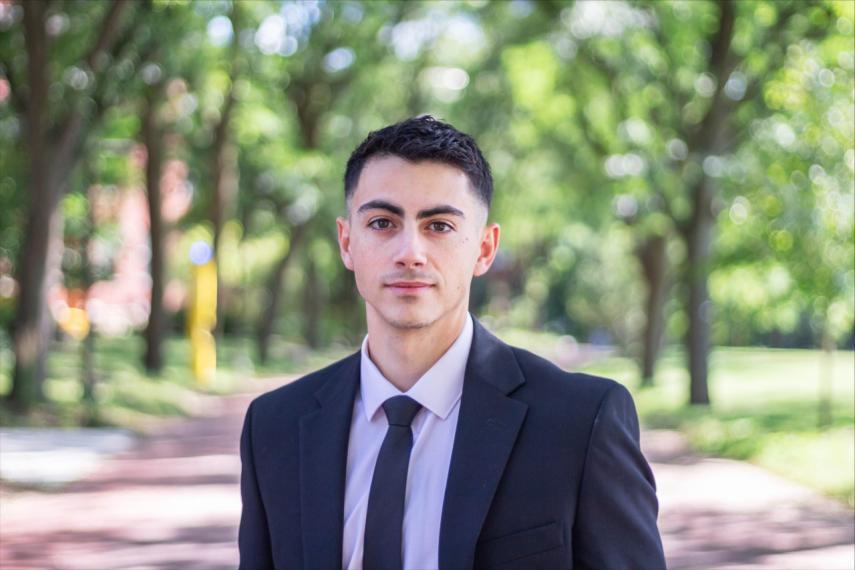 Image of Lorenzo in a suit on campus, with trees in the background