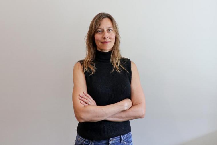 Kathryn Preuss standing and smiling against neutral backdrop with arms crossed