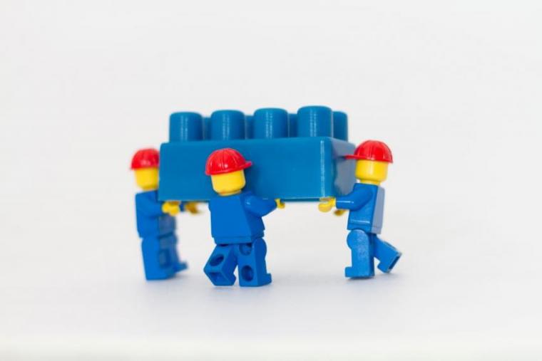 Three LEGO construction figurines carrying a LEGO brick