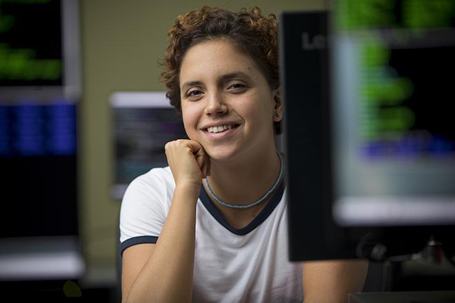 Image of student looking at camera from behind computer and smiling