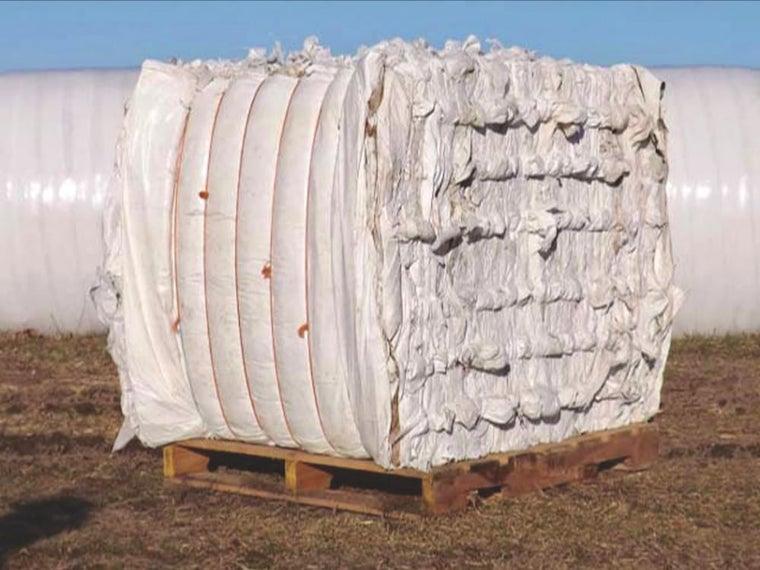 A large bale of plastic rests on a wooden crate on the grass at a farm