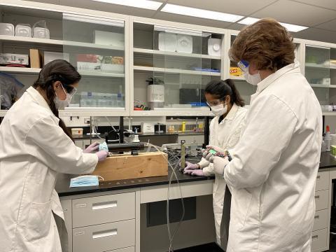 Three scientists in lab coats working on a device 