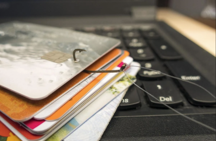 Stack of credit cards on a laptop with a fishing hook through one.