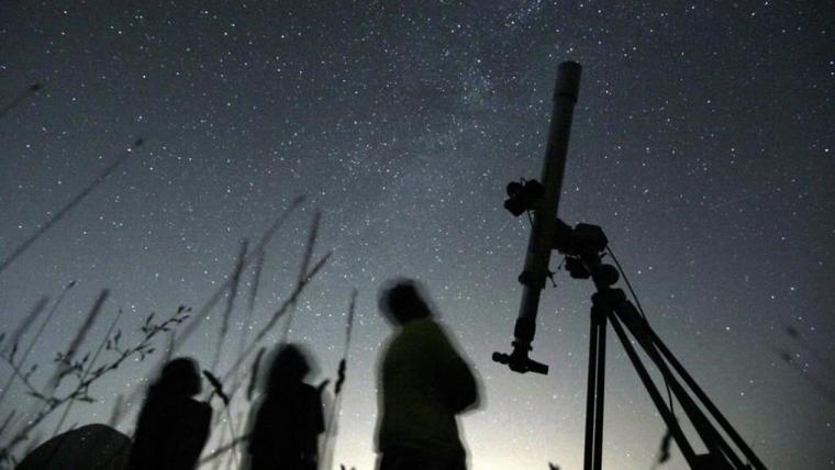 Silhouette of a telescope and three people looking up at the starry night sky.