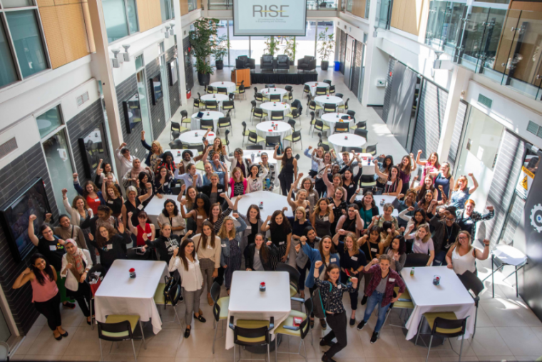 Group of RISE 2023 attendees looking up at the camera with arms raised.