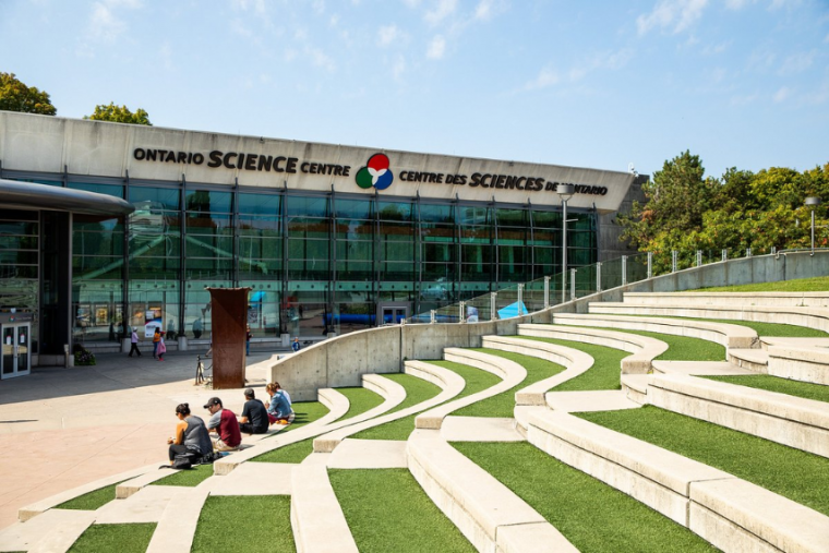 Ontario Science Centre in the summer with three people sitting on the steps.