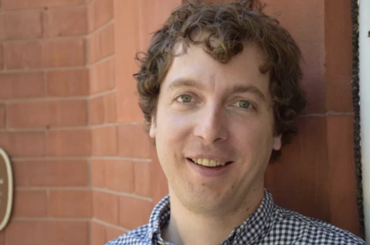 A picture of a man smiling in front of a brick wall