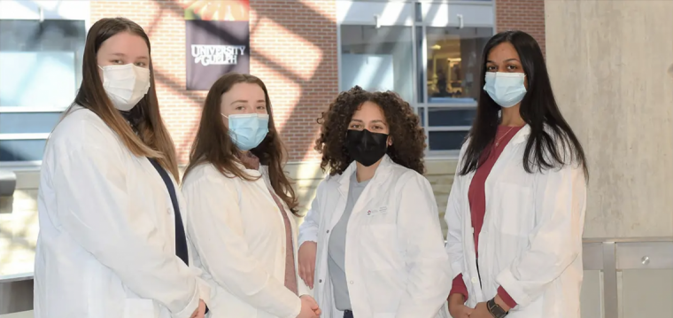 Image of four women in white lab coats with masks on looking at the camera.