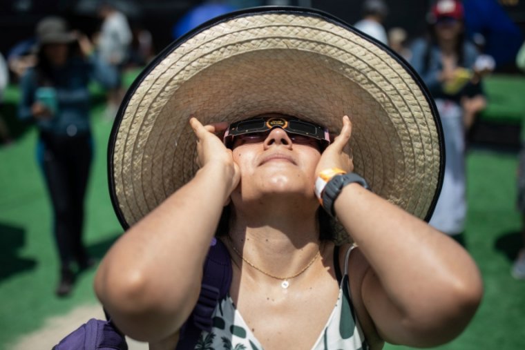 Woman in large straw hat and sunglasses looks up to sky at a supposed eclipse. 