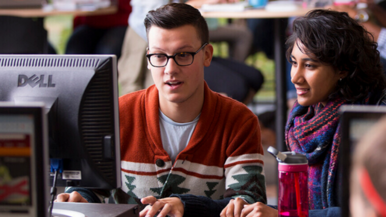 Two students in a computer lab, both examining a screen.